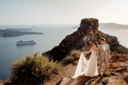 Sesja ślubna na Santorini – magia, emocje i światło, którego nie da się podrobić 2 para młoda spacerująca po skałach z widokiem na Skaros Rock i kalderę – Santorini