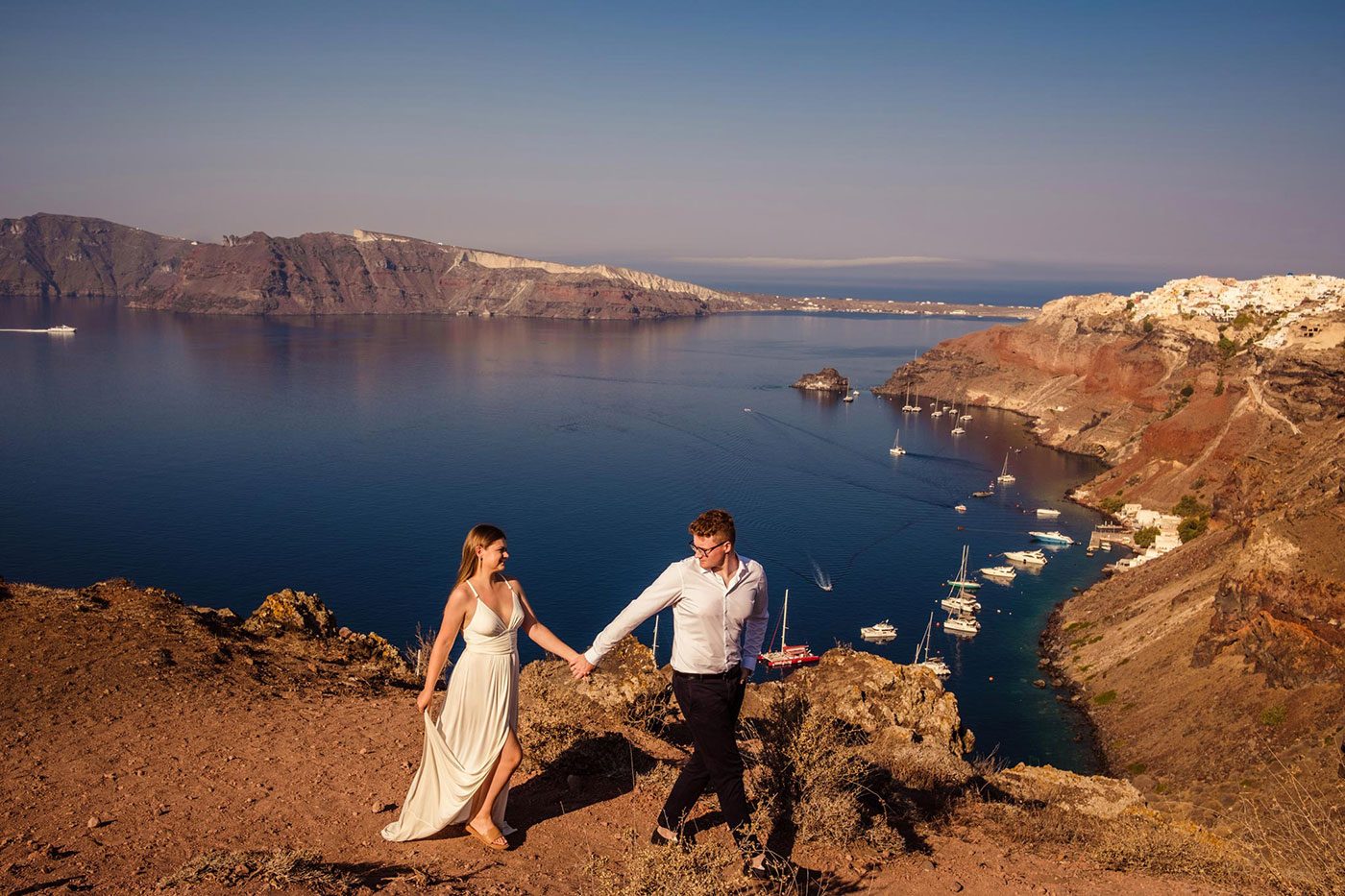 para młoda spacerująca po skałach na tle morza i białych domków – Oia, Santorini